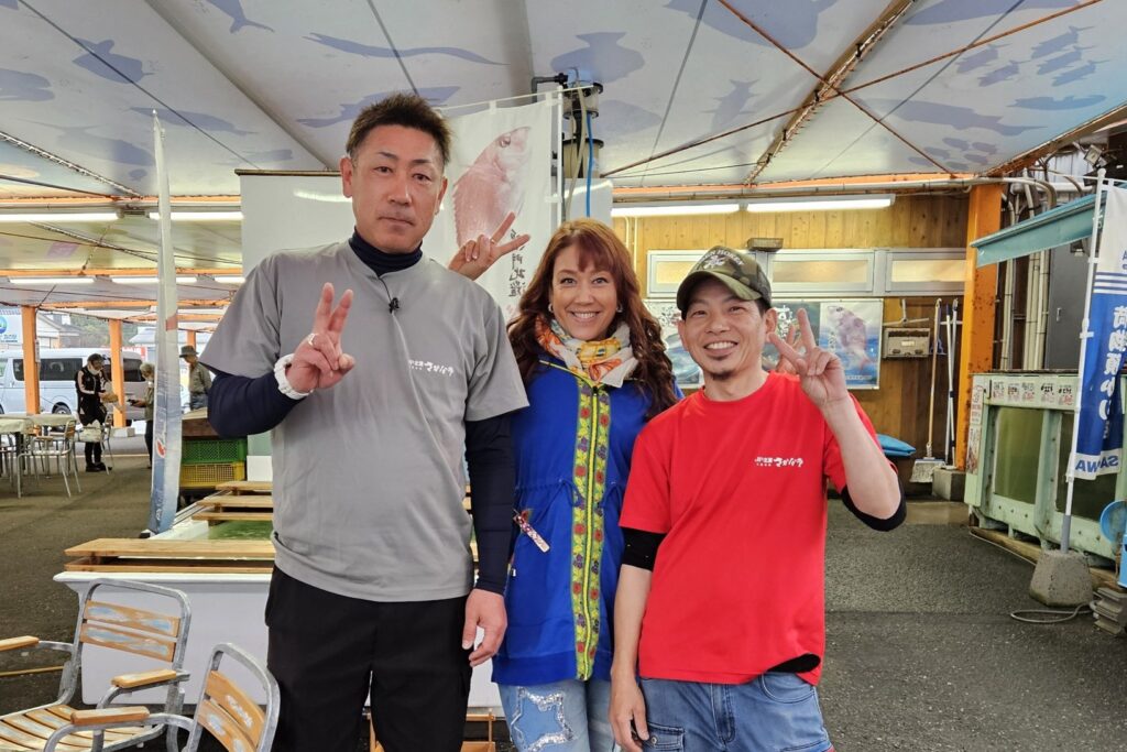 さかな市の店内で、LiLiCoさんとさかな市のスタッフ2人が並んでピースをしている写真